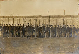 Retrato de un grupo militar en formación y su mando, pertrechados con palos. Fotógrafo desconocido.